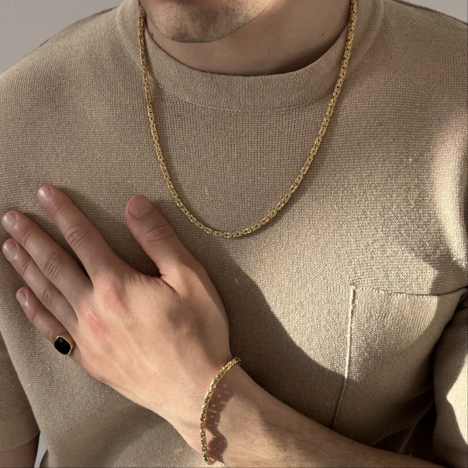 Königskette und Königsarmband aus vergoldetem 925 Sterling Silber – stilvoll getragen auf beigefarbenem Pullover, kombiniert mit goldfarbenem Siegelring – eleganter Herrenschmuck im Sonnenlicht