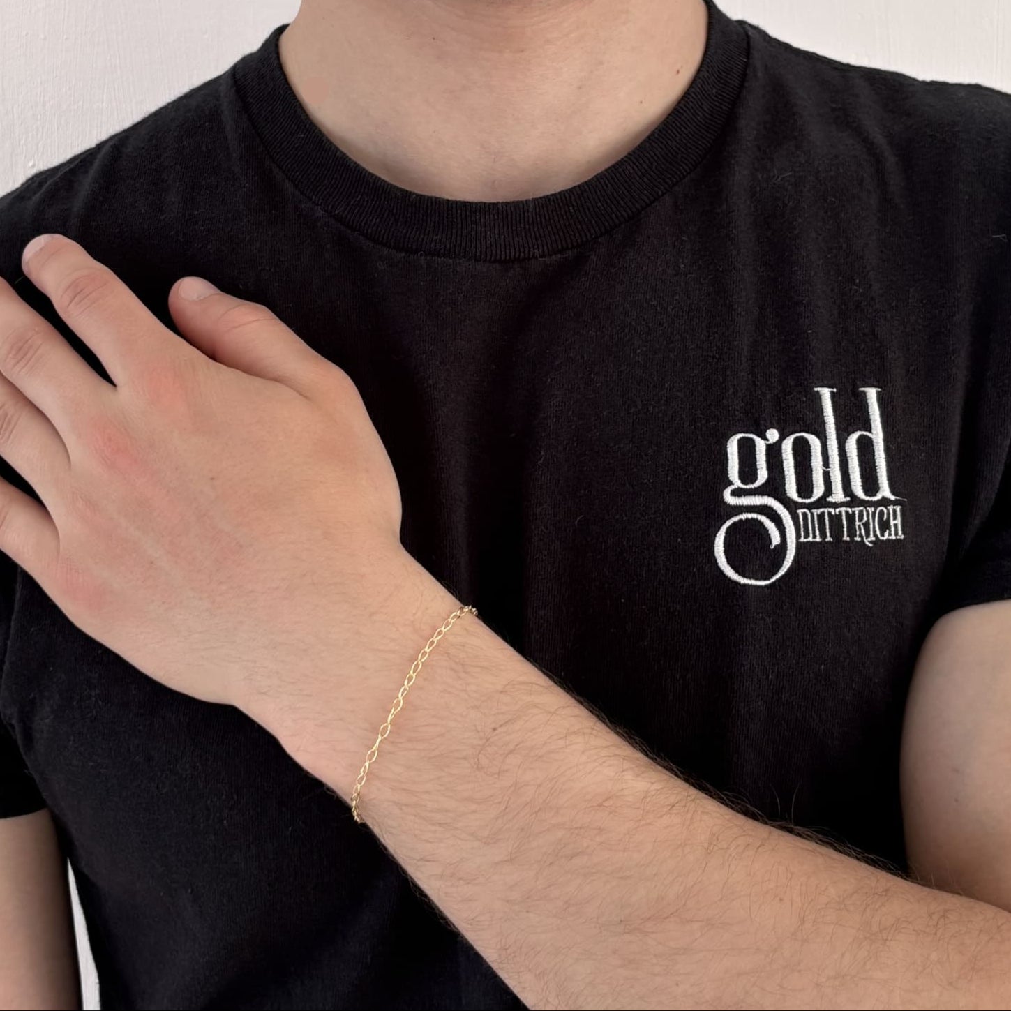 Mann mit schwarzem Gold Dittrich Shirt trägt ein filigranes Weitankerarmband aus 375er Gelbgold – zartes, elegantes Design mit ca. 19 cm Länge und Karabinerverschluss.