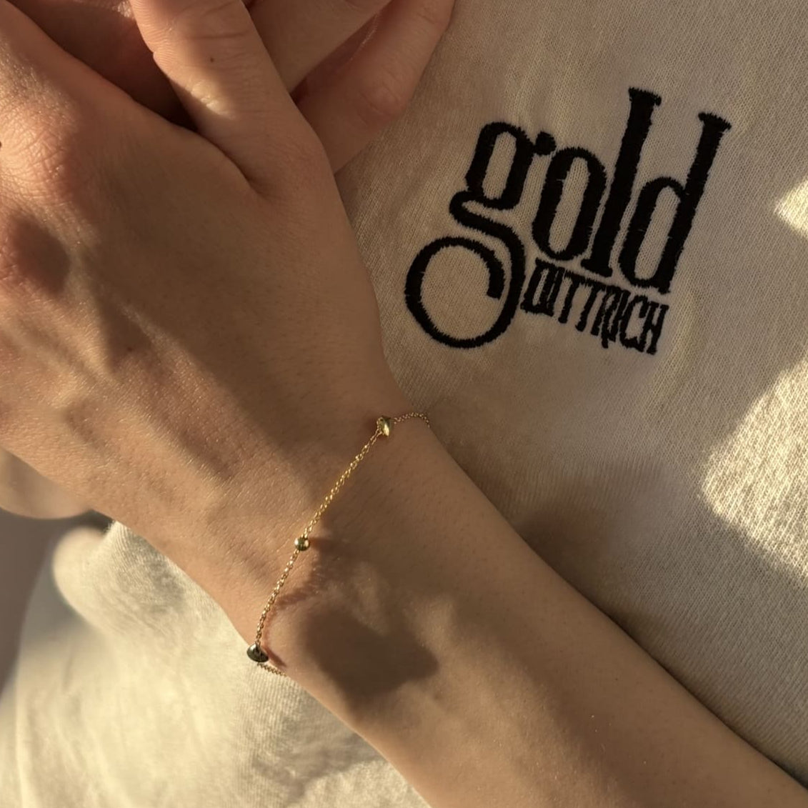 Zartes vergoldetes Armband aus 925 Sterling Silber mit Herz- und Kugel-Elementen, getragen von einer Frau im Gold Dittrich Shirt – feines Ankerkettchen mit femininer Ausstrahlung.