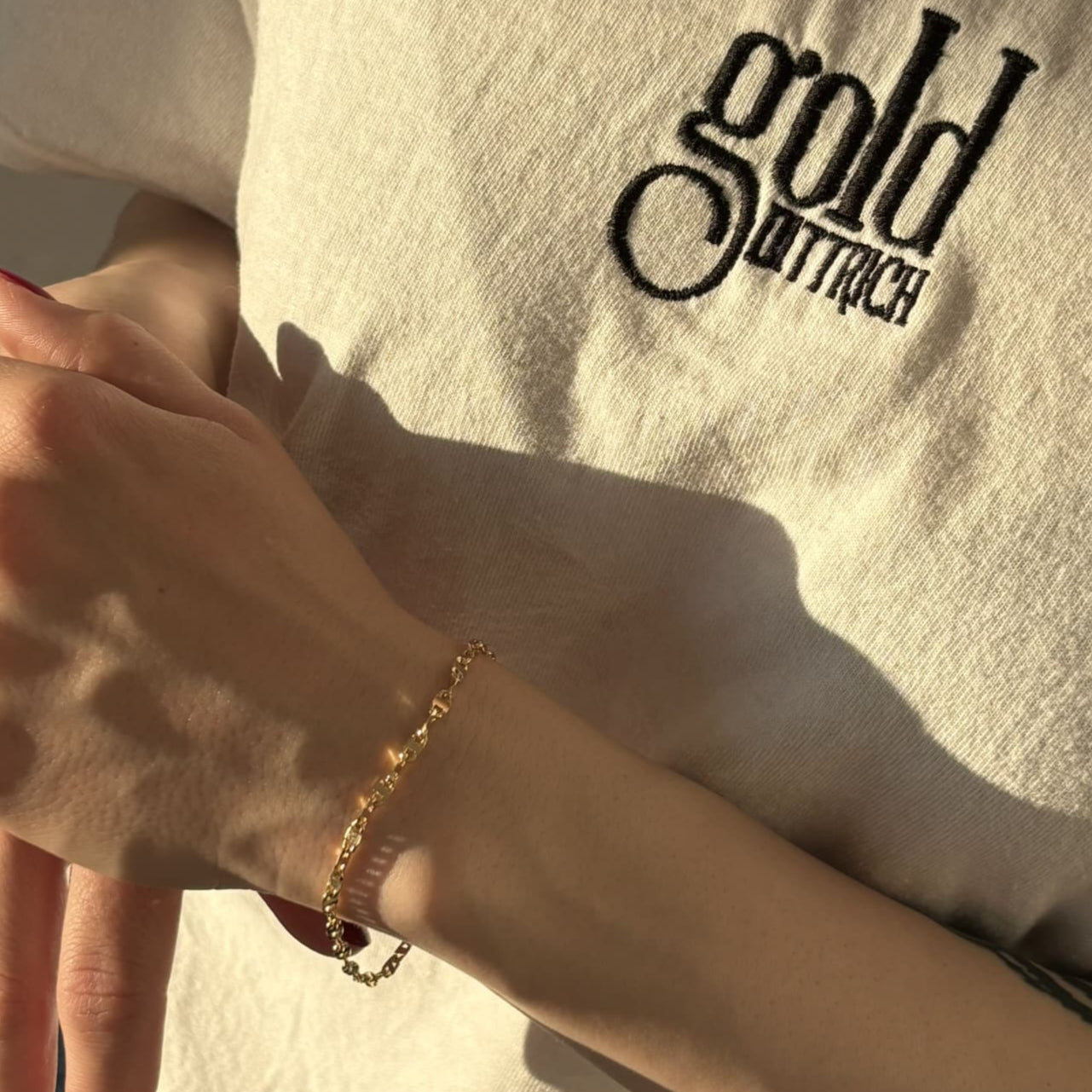Nahaufnahme eines Armbands aus 585er Gelbgold in Panzerkettenoptik am Handgelenk einer Frau – glänzender Goldschmuck getragen zu einem weißen Gold Dittrich Shirt im warmen Sonnenlicht.