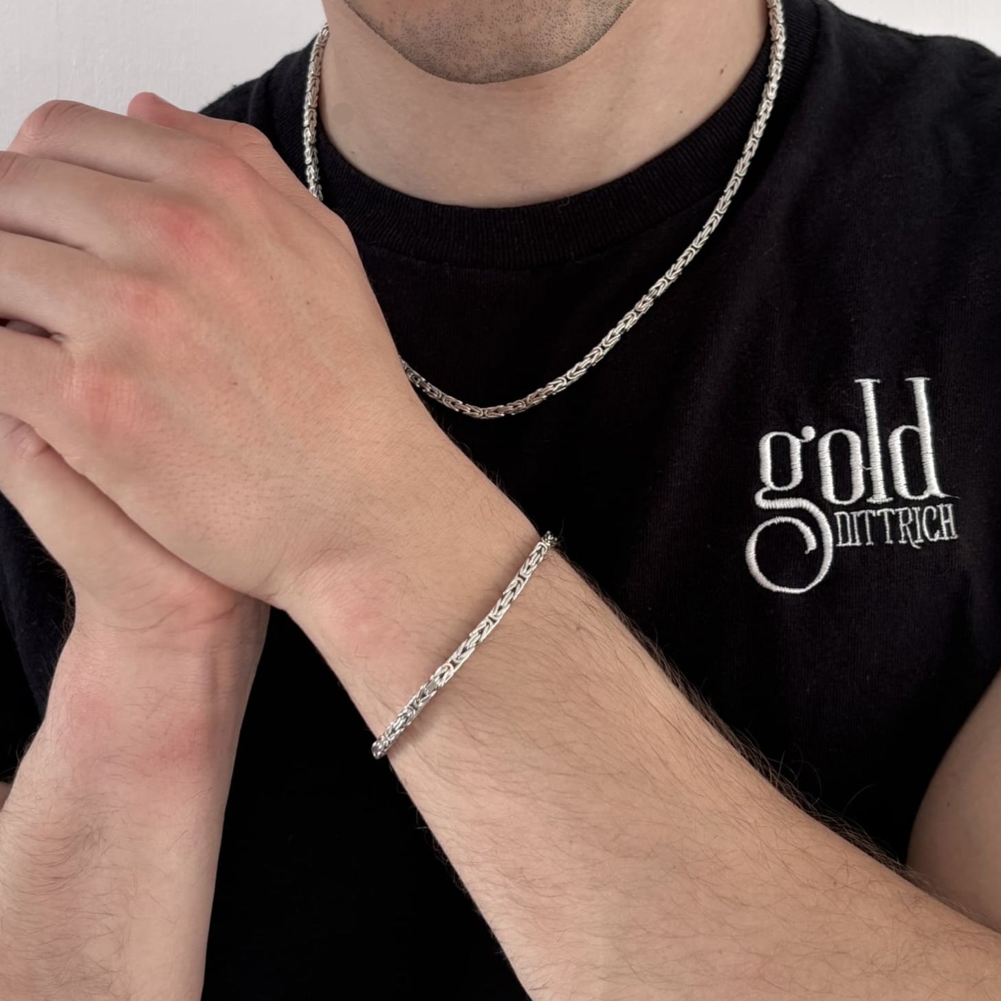 Herr mit schwarzem Gold Dittrich Shirt trägt ein rhodiniertes Königsarmband aus 925 Sterling Silber am Handgelenk – kombiniert mit passender Silberkette für einen stilvollen, modernen Look.
