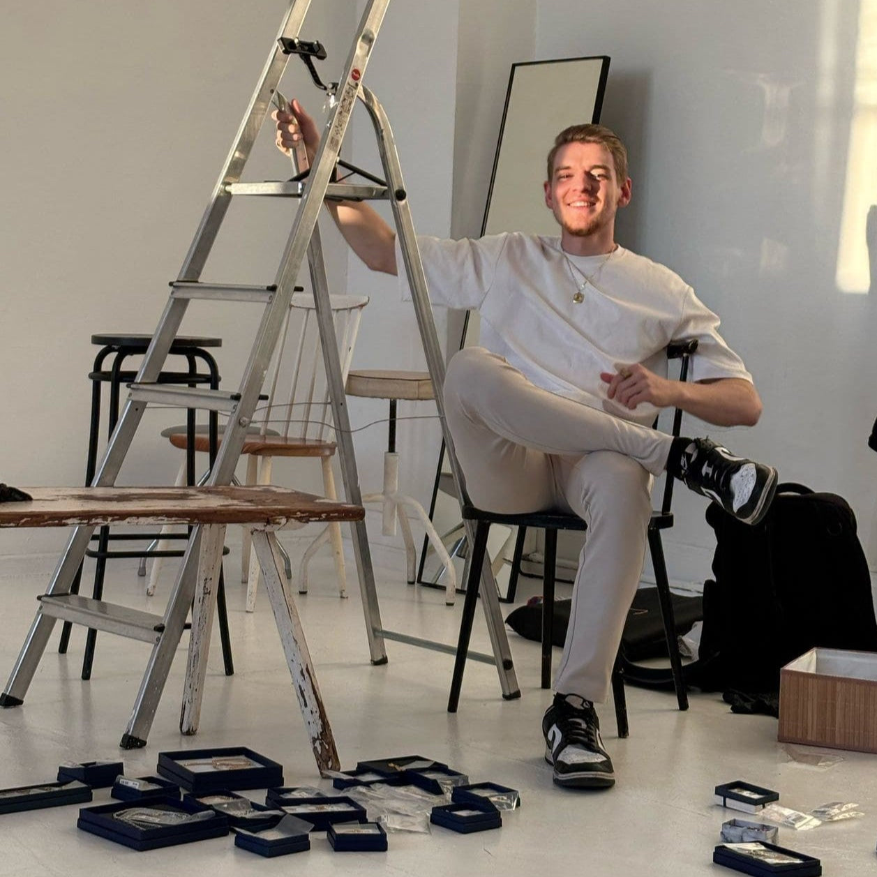 Der Gründer von Gold Dittrich sitzt entspannt beim Fotoshooting mit ausgebreiteten Schmuckstücken – Making-of-Moment in kreativem Studio mit persönlichem Einblick hinter die Kulissen.