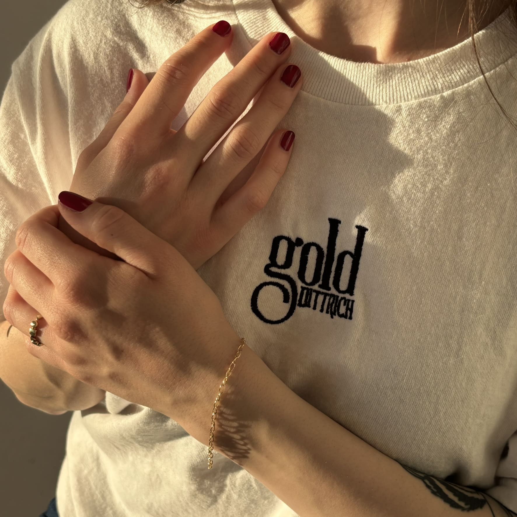 Frau mit weißem Gold Dittrich Shirt und rotem Nagellack trägt ein filigranes Ankerarmband aus 375er Gelbgold – zarter, eleganter Armschmuck für Damen in weiter Gliederung.