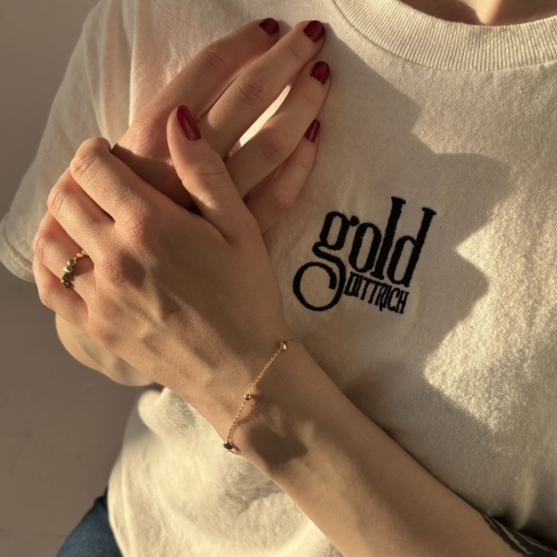 Zartes vergoldetes Armband aus 925 Sterling Silber mit Herz- und Kugel-Elementen, getragen von einer Frau im Gold Dittrich Shirt – feines Ankerkettchen mit femininer Ausstrahlung.