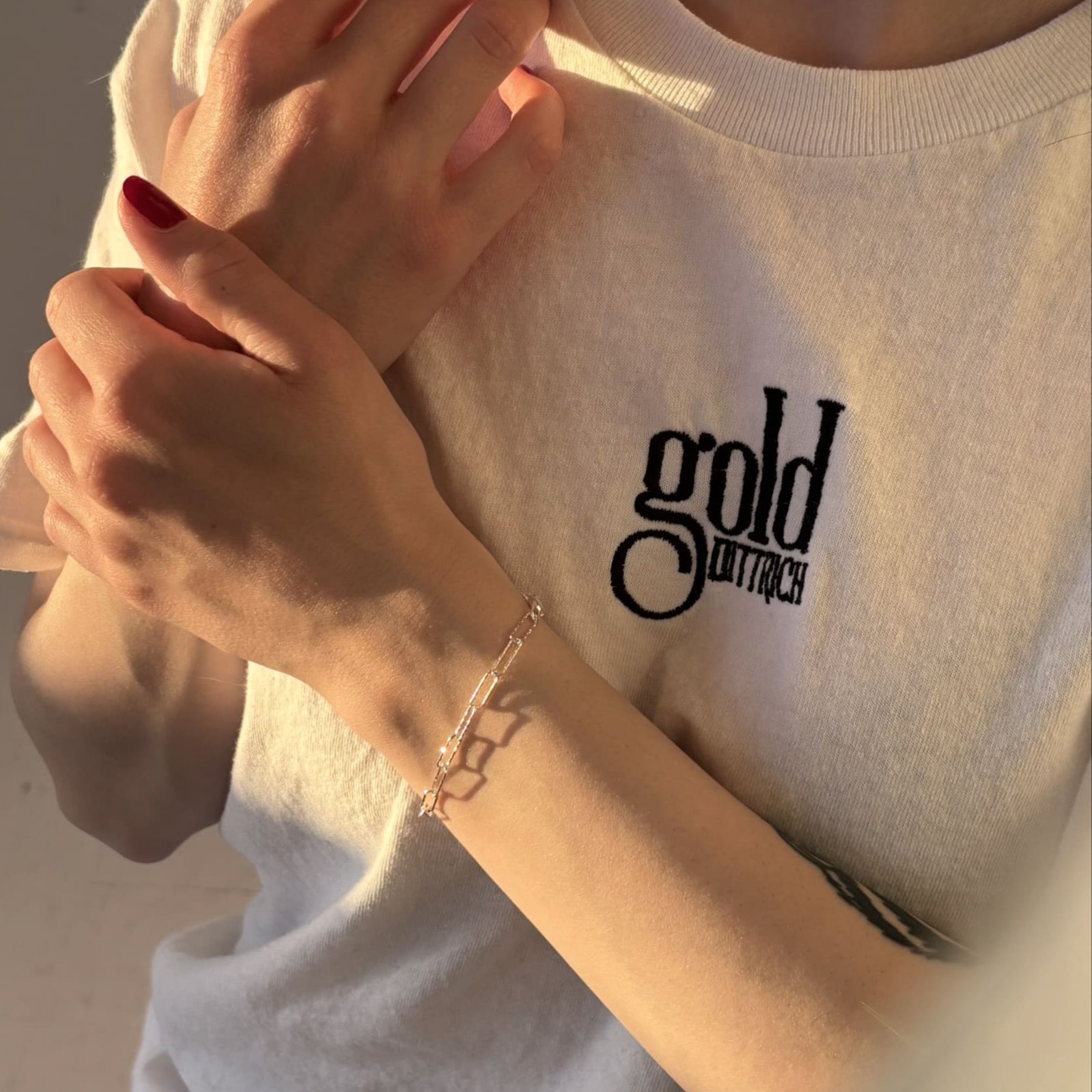 Nahaufnahme eines diamantierten Damen-Armbands aus 925 Sterling Silber am Handgelenk – getragen zu einem weißen T-Shirt mit Gold Dittrich Logo, eingefangen im warmen Sonnenlicht.