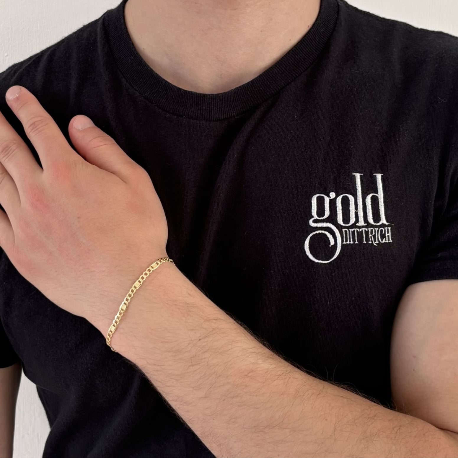 Mann mit schwarzem Gold Dittrich Shirt trägt ein filigranes Armband aus 333er Gelbgold am Handgelenk – dezentes Gliederdesign mit Karabinerverschluss für stilvolle Alltagslooks.