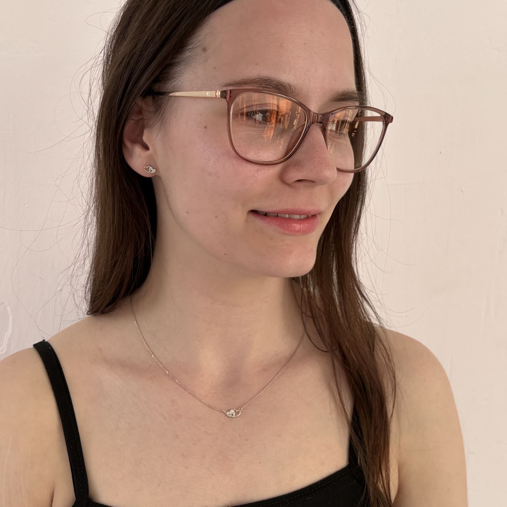 Frau mit Brille trägt ein zartes Schmuckset aus rhodiniertem 925 Sterling Silber mit Herzanhänger und passenden Ohrsteckern – romantischer Damenschmuck in filigranem Design von Gold Dittrich.